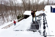 Mike McKechnie of Mountain View Solar and Wind sweeping teh snow off the solar panels on top of the house of William Sedlacek (in red jacket on the deck below) in Great Cacapon.